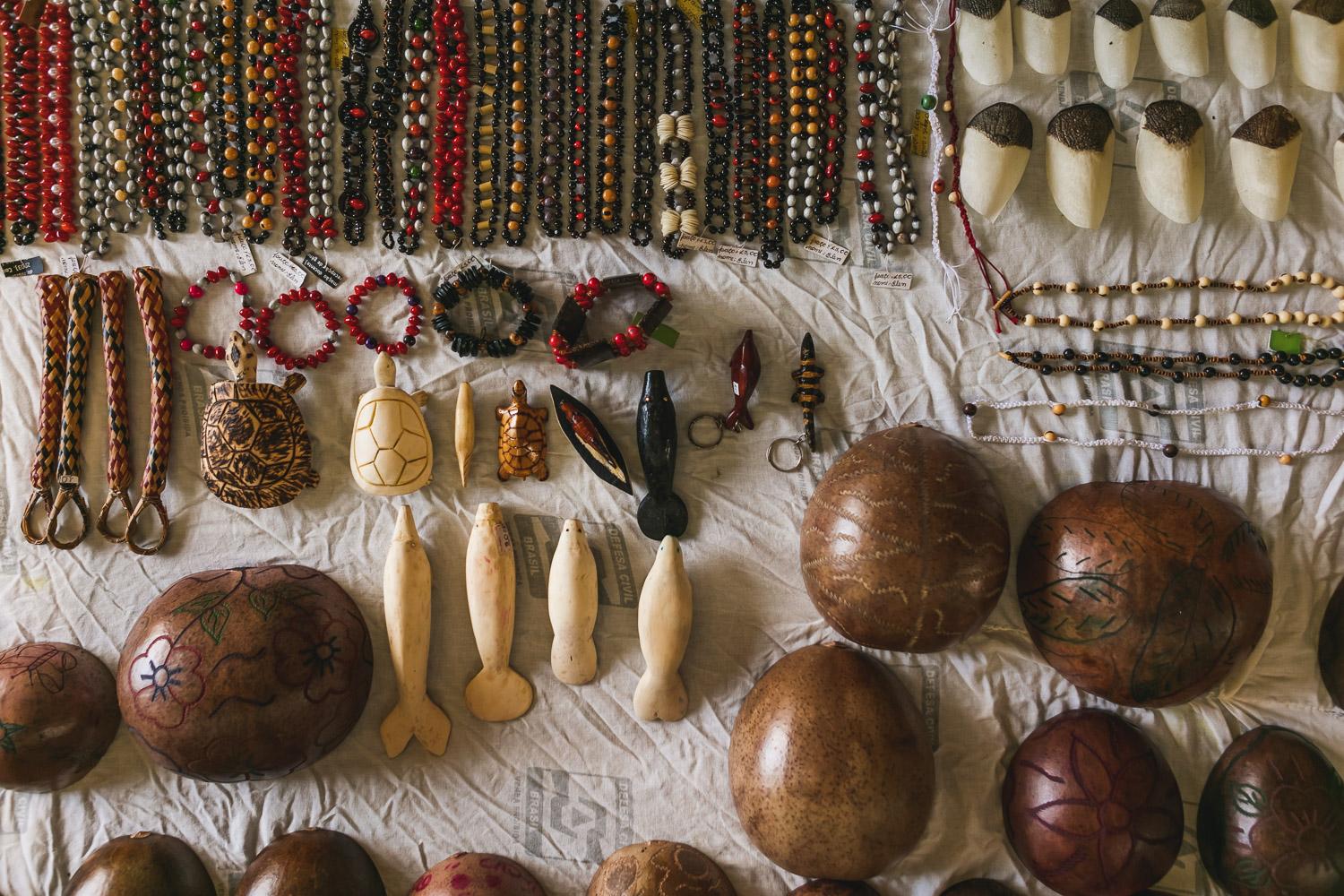 Traditionelles indigenes Kunsthandwerk aus dem Amazonas Auswahl handgefertigter indigener Kunstobjekte wie Schmuck, geschnitzte Figuren und verzierte Kalebassen auf einem weißen Tuch ausgebreitet