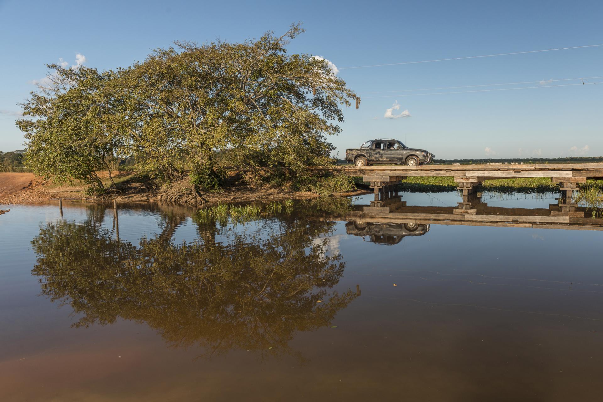 Fahrt über eine Holzbrücke im Pantanal – Naturerlebnis in Brasilien. Pickup auf einer Holzbrücke im Pantanal mit Spiegelung der Landschaft im Wasser.
