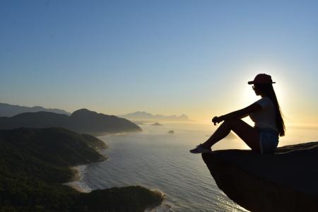 Frau sitzt im Sonnenaufgang auf dem Pedra do Telégrafo mit Blick auf die Küste von Rio de Janeiro