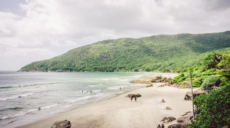 Blick auf den Praia do Matadeiro in Florianópolis mit weißem Sandstrand, grünen Hügeln und sanften Wellen