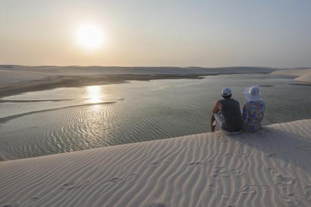 Sonneuntergang über einem See und zwei Menschen im Vordergrund auf einer Düne sitzend